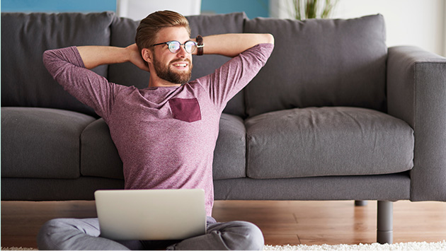 Man with laptop sitting on floor near couch at home