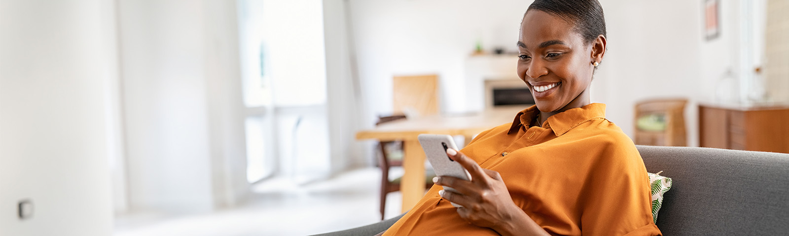 Wideshot of pregnant woman using her phone on the couch